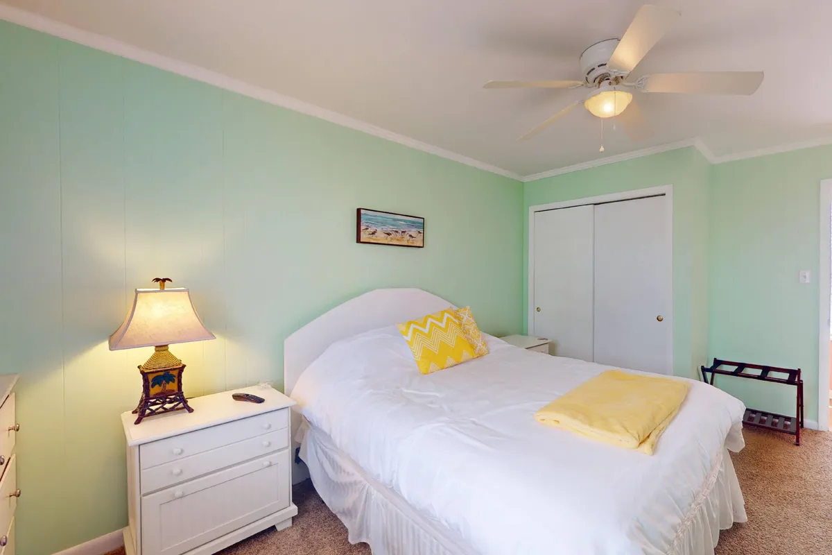 A serene bedroom with a comfortable bed dressed in crisp linens, a bedside lamp casting warm light, cheerful yellow accents, and calming artwork. The room is filled with gentle morning light, and the tranquil atmosphere invites deep rest and relaxation.