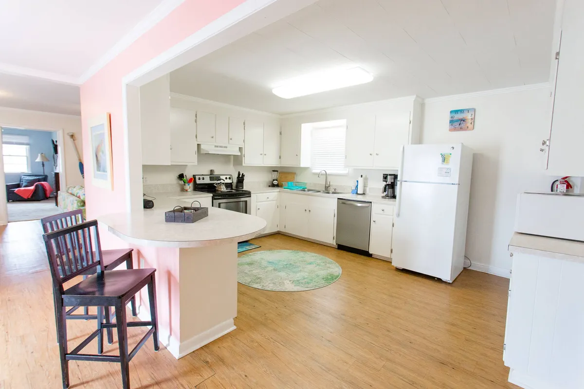 A bright kitchen scene showing a central kitchen island surrounded by stools, modern appliances, and a colorful rug, creating a cheerful and lively space. The setup encourages both cooking and socializing, with the breakfast counter ideal for enjoying morning coffee or casual meals.