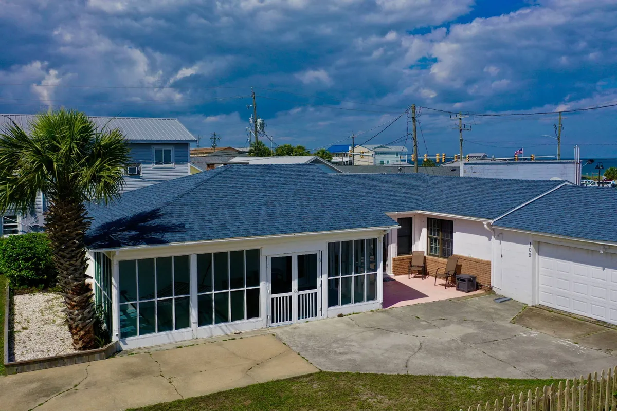 Exterior shot of a welcoming cottage, featuring a screened porch with comfortable outdoor seating, a palm tree, and a driveway. The porch overlooks nature, hinting at relaxed mornings or evenings spent together after a day of exploring, all within a single-level, accessible layout.
