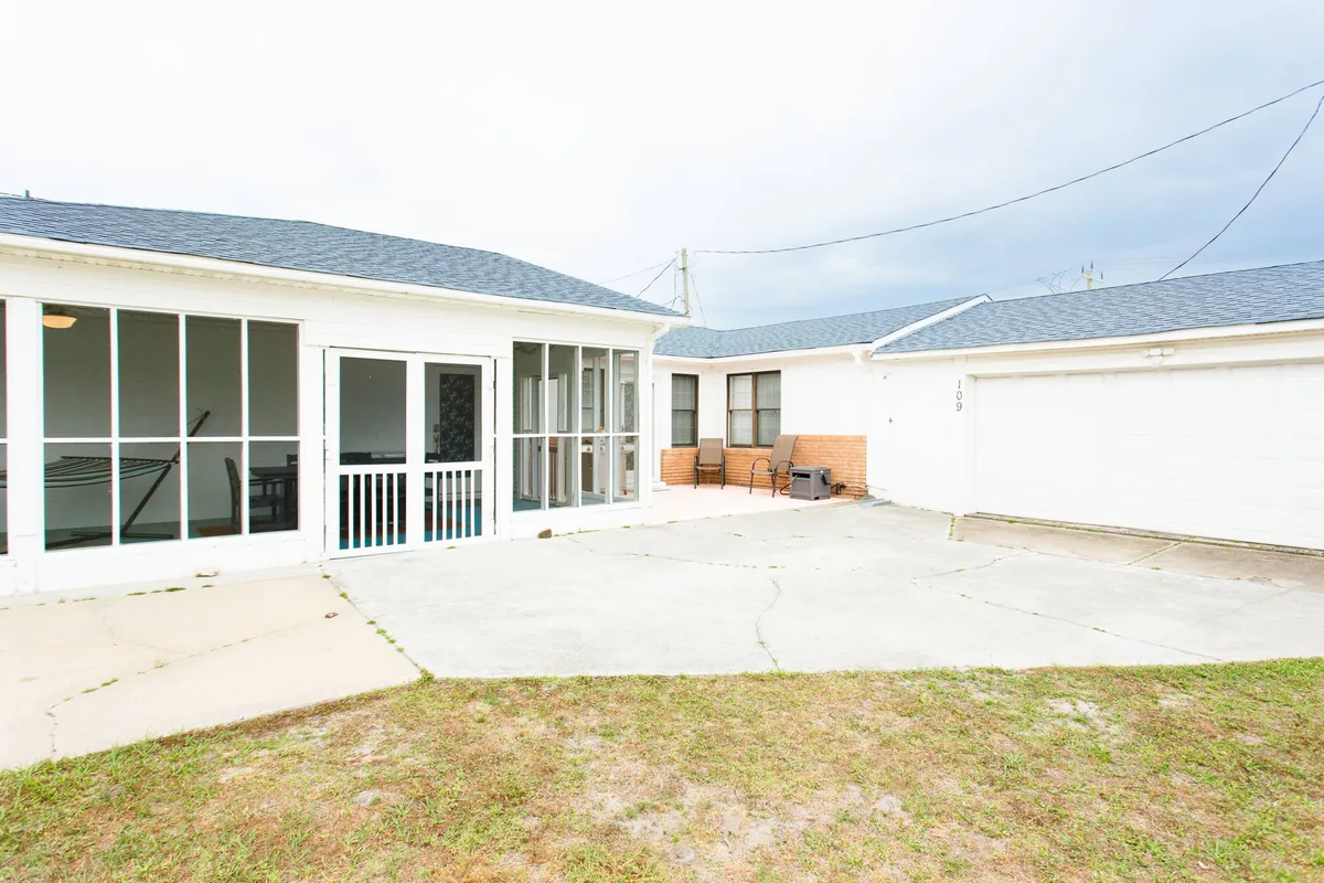 This image depicts the inviting screened porch and adjacent patio area, featuring comfortable outdoor seating and a view of the garage. The setting suggests a breezy, relaxed atmosphere ideal for socializing, dining, or simply enjoying the outdoors in comfort.