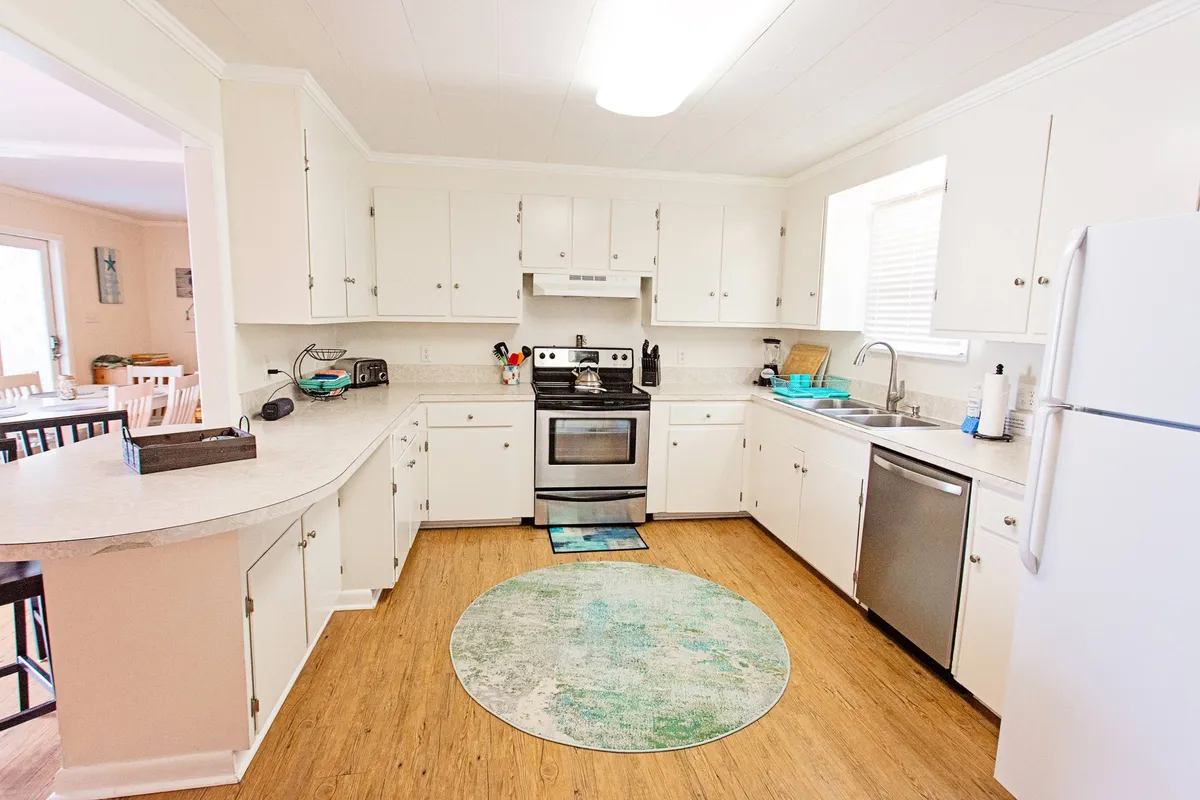 A welcoming kitchen featuring stainless steel appliances, a spacious kitchen island with a circular rug beneath, and ample counter space. The vibe is warm and inviting, perfect for cooking and spending time with family and friends. Visible utensils and cookware suggest the kitchen is fully equipped and ready for a variety of meal preparations.