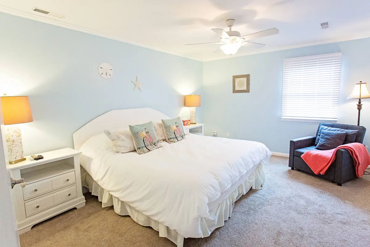 A spacious, serene bedroom features a large bed with decorative pillows, a cozy armchair, and soft lighting from bedside lamps. The room radiates comfort and intimacy, ideal for both relaxing evenings and restful nights.