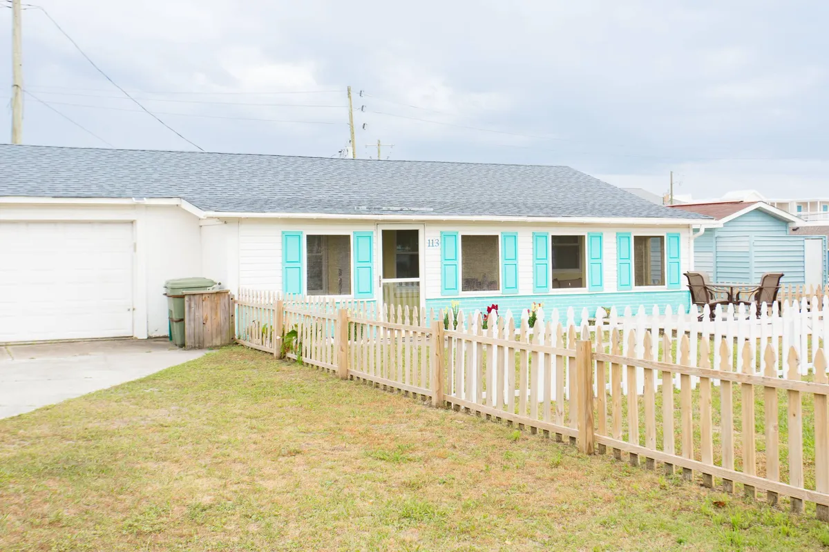 This image showcases a friendly, pet-welcoming exterior with white picket fencing, a green lawn, and an outdoor seating area. The fenced yard is visible, suggesting a secure, open space ideal for children and pets to play safely.
