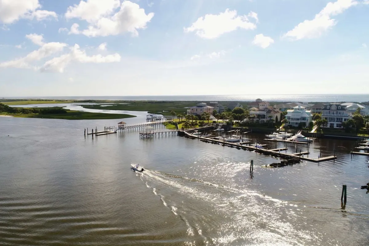 A tranquil marina scene featuring calm waterways, docked boats, and houses along the shore. The setting sun casts a warm glow, highlighting the serene beauty and recreational potential of the area for boating, kayaking, and fishing.