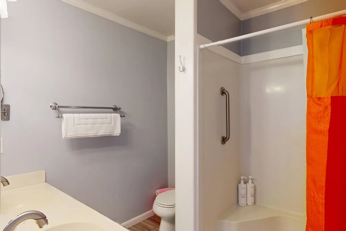 A bright, functional bathroom with a sink, shower, toilet, and towel rack. The clean and inviting design ensures easy routines, while thoughtful touches like a shower curtain and towel placement offer a sense of homey comfort.