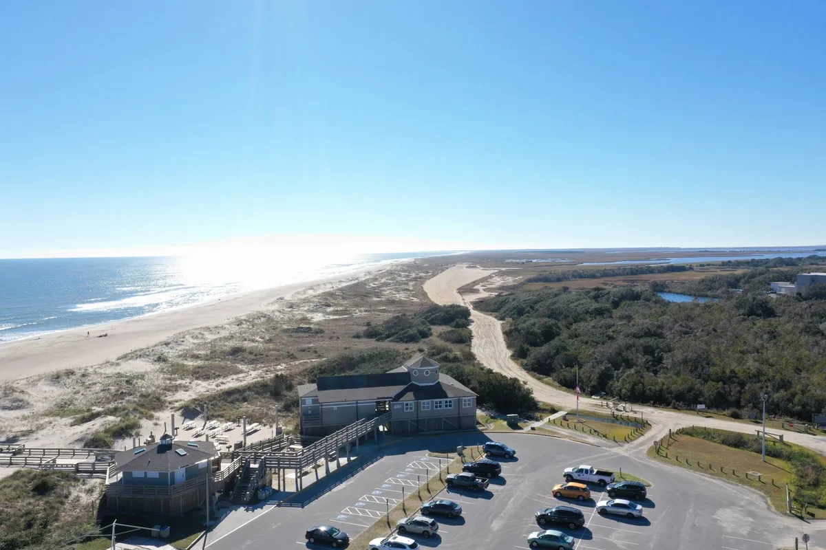 This image captures the beach, ocean, parking lot, and the building, showing the easy access from the property to the coastline. The relatively flat terrain and direct path from parking to the sand highlight accessibility for all guests.