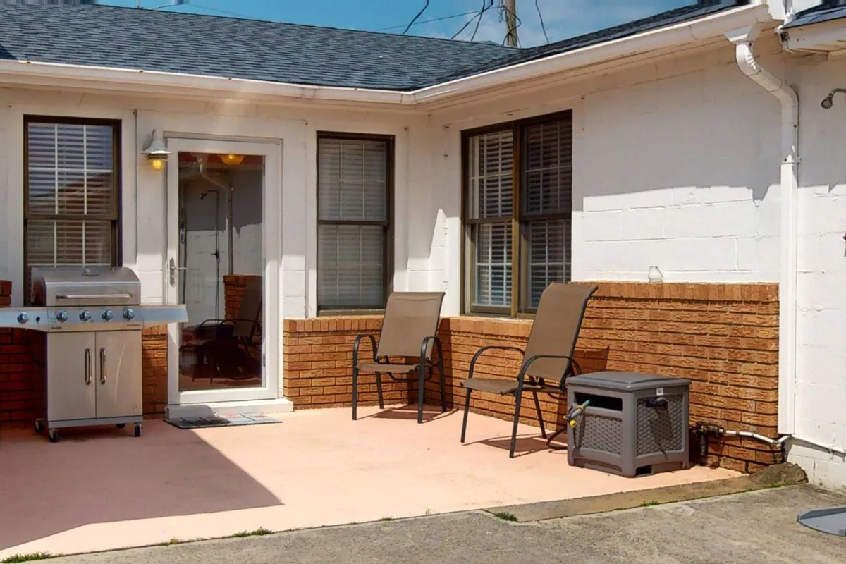 A cozy exterior patio area featuring an outdoor grill and two comfortable chairs, perfect for relaxing or entertaining after a day at the beach. The inviting setup suggests a seamless transition from outdoor adventures to laid-back evenings.